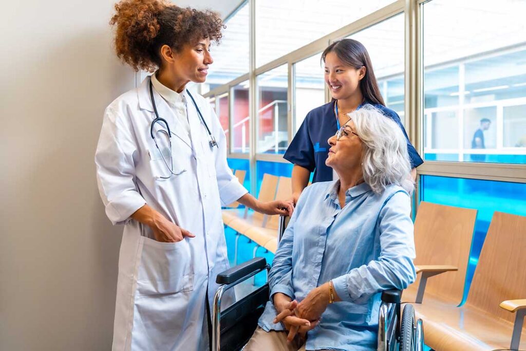 An older adult sits at a table completing a puzzle while a caregiver offers gentle assistance.